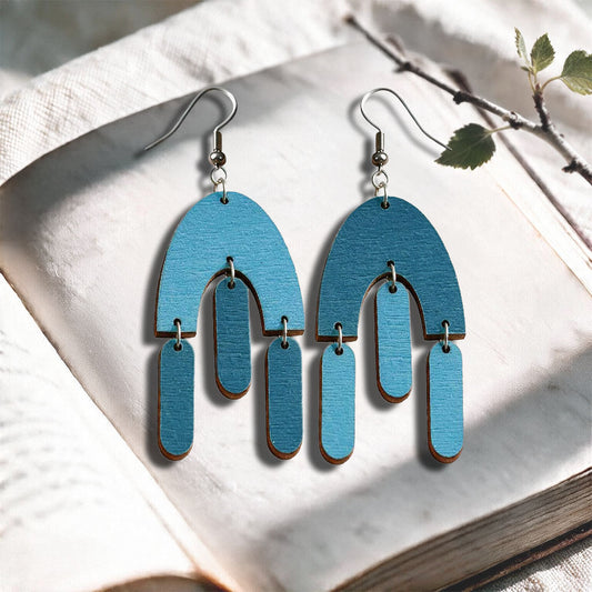 Sky blue and pertol Fluttering Hems plywood earrings made in Finland, photographed on a vintage book in natural sunlight