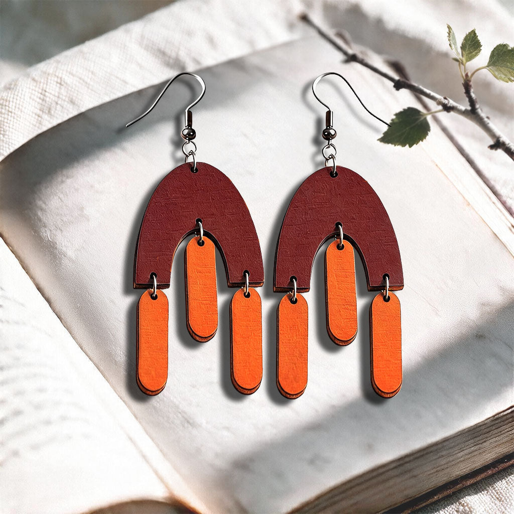 Orange and brown Fluttering Hems plywood earrings made in Finland, photographed on a vintage book in natural sunlight