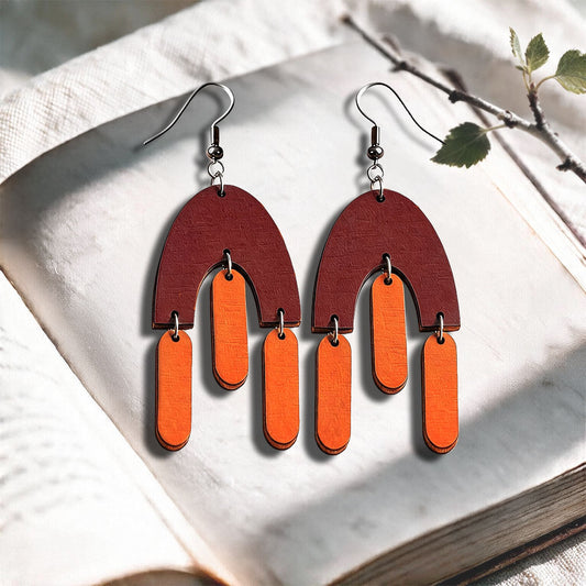 Orange and brown Fluttering Hems plywood earrings made in Finland, photographed on a vintage book in natural sunlight