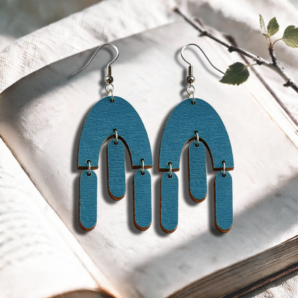 Petrol Fluttering Hems plywood earrings made in Finland, photographed on a vintage book in natural sunlight