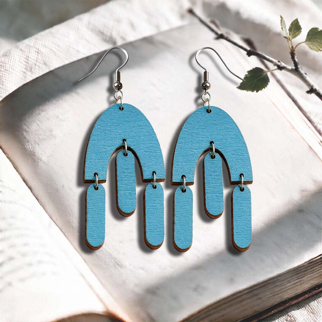 Skyblue Fluttering Hems plywood earrings made in Finland, photographed on a vintage book in natural sunlight