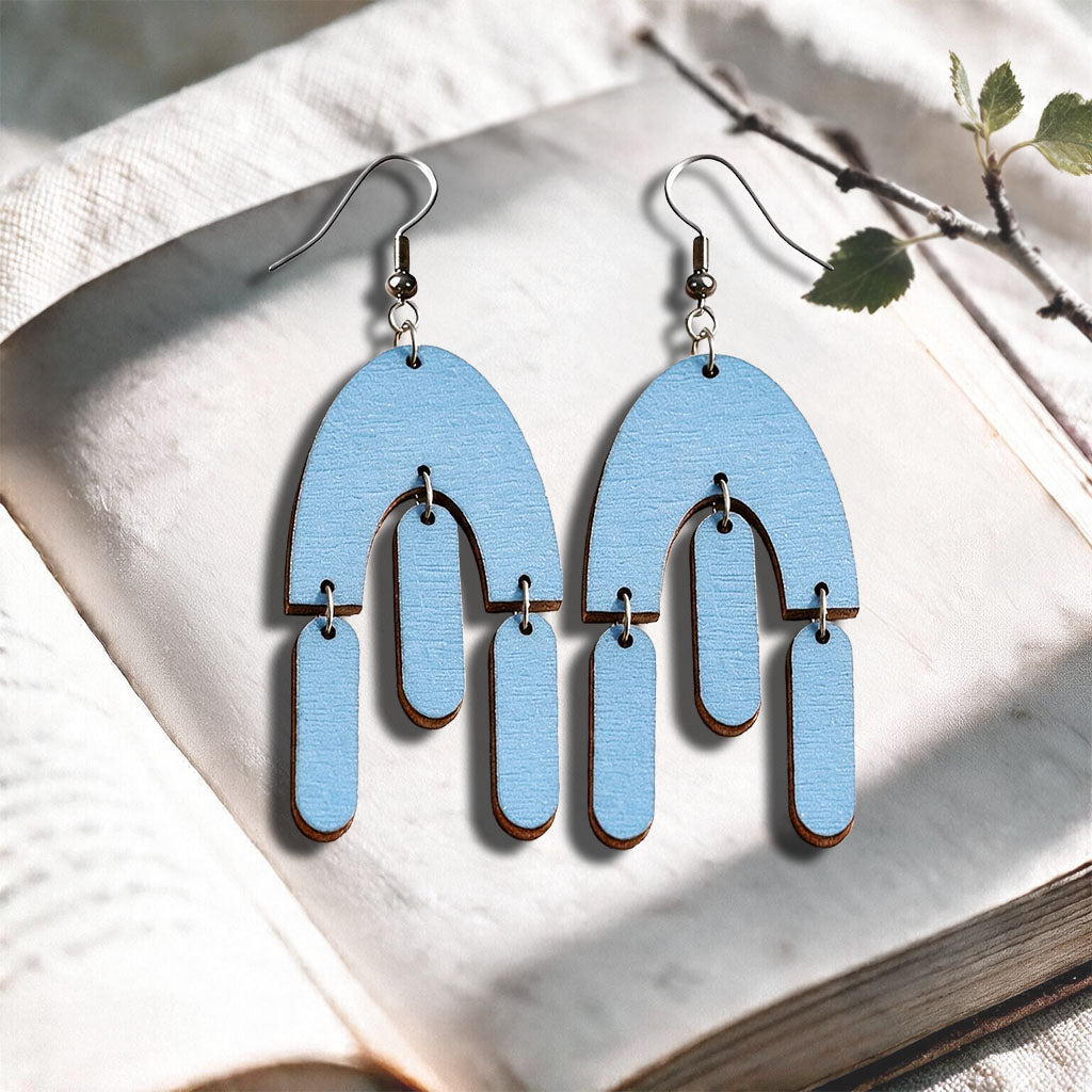 Lightblue Fluttering Hems plywood earrings made in Finland, photographed on a vintage book in natural sunlight