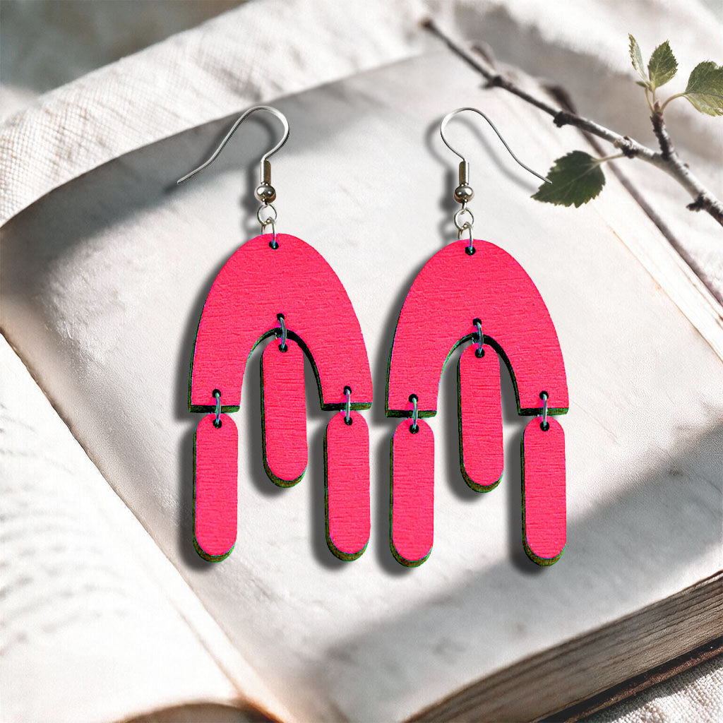 Raspberry Fluttering Hems plywood earrings made in Finland, photographed on a vintage book in natural sunlight