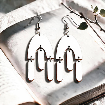 White Fluttering Hems plywood earrings made in Finland, photographed on a vintage book in natural sunlight