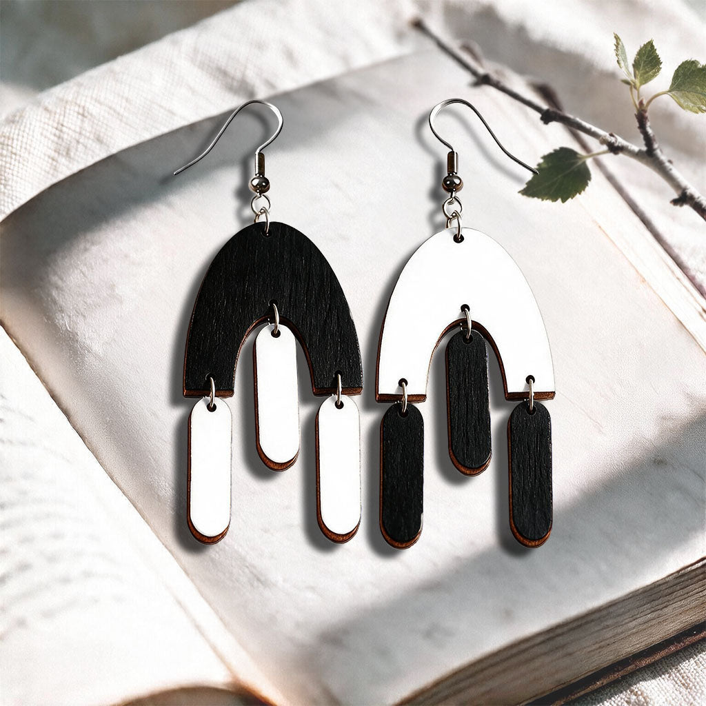 Black and white Fluttering Hems plywood earrings made in Finland, photographed on a vintage book in natural sunlight
