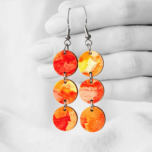 Red, orange and yellow Leimahdus (Flame) plywood earrings with hand-blown ink patterns, made in Finland, photographed against a black and white background of a hand.