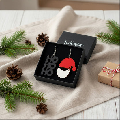 HO HO HO and Santa Claus earrings presented in a gift box with pine branches, pinecones, and a wrapped present, creating a cozy Christmas atmosphere. Handmade in Finland by byMinta.