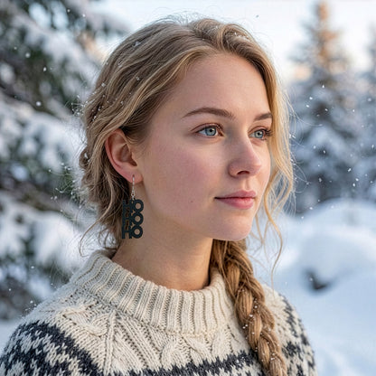 Blonde woman wearing the HO HO HO earring in a snowy winter landscape, dressed in a warm Nordic knit sweater. Handmade in Finland by byMinta.