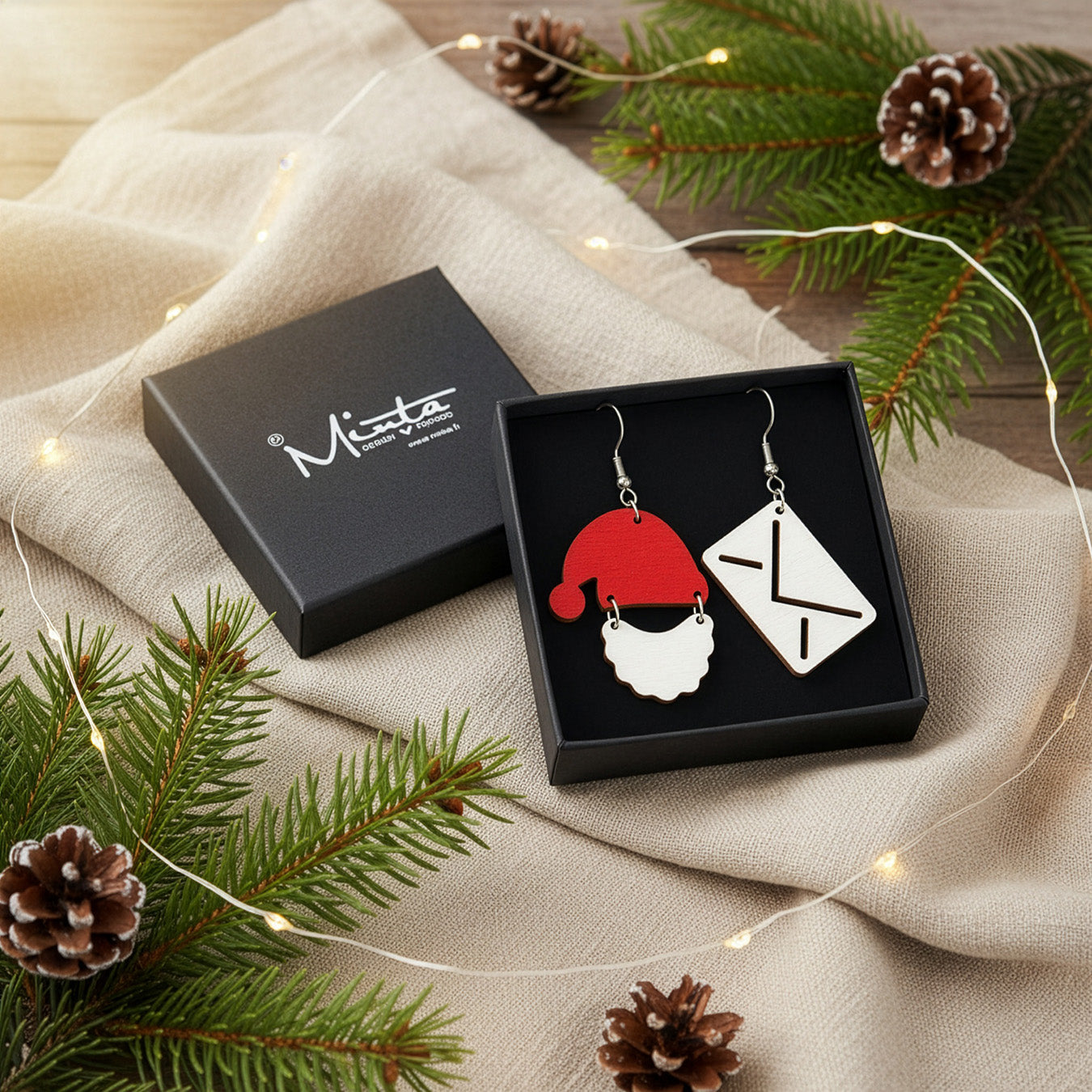 Christmas earrings presented in a gift box with pine branches, pinecones, and warm fairy lights, creating a festive holiday atmosphere. Handmade in Finland by byMinta.
