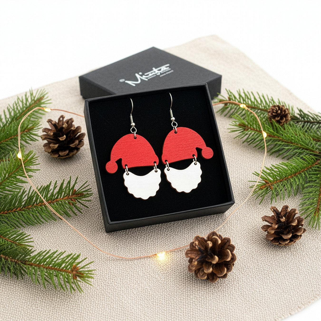 Santa Claus earrings presented in a gift box with pine branches, pinecones, and soft lights, creating a festive Christmas atmosphere. Handmade in Finland by byMinta.