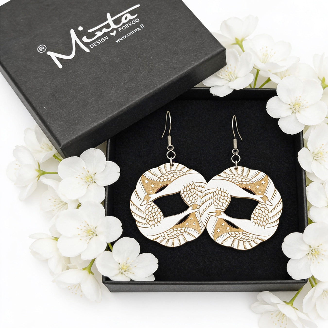 Handmade light wood statement earrings displayed in a black jewelry gift box surrounded by delicate white flowers. Bright soft natural light, elegant Nordic style product photography with airy and romantic atmosphere.