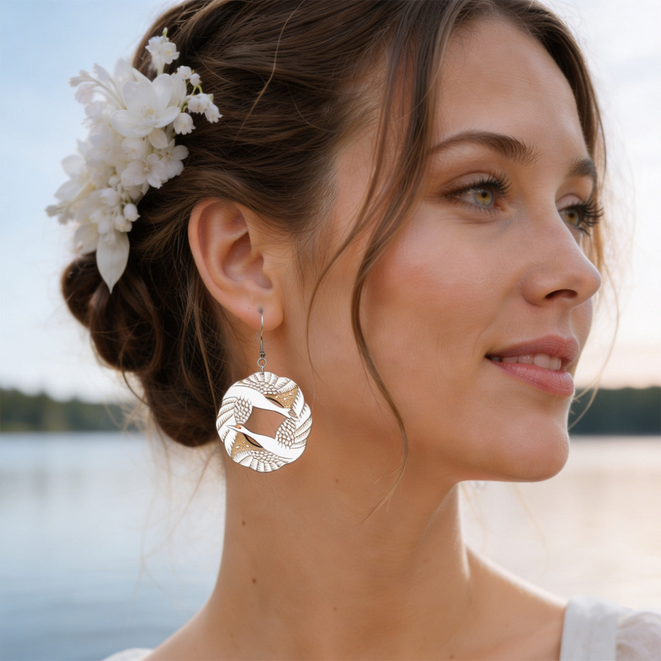 Elegant portrait of a woman by the lake wearing handmade light wood statement earrings with leaf pattern details. Soft natural light, white flowers in her hair, calm Nordic summer atmosphere.