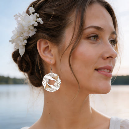 Elegant portrait of a woman by the lake wearing handmade light wood statement earrings with leaf pattern details. Soft natural light, white flowers in her hair, calm Nordic summer atmosphere.