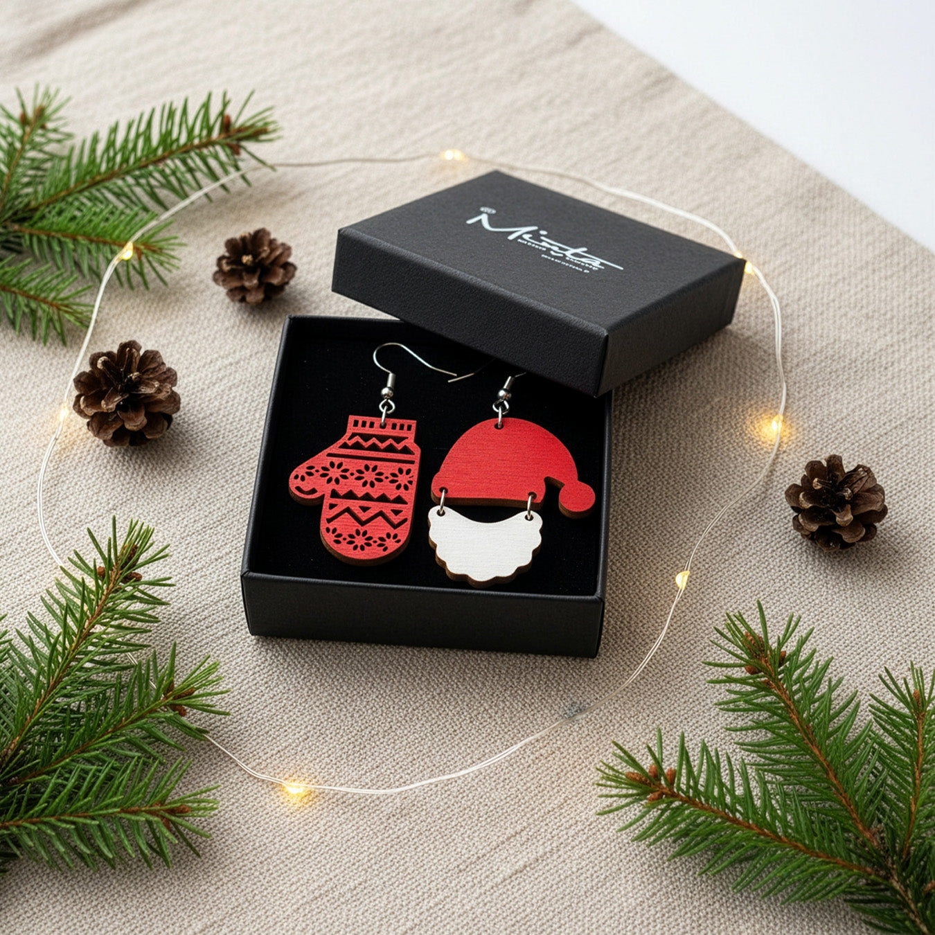 Christmas earrings presented in a gift box with pine branches, pinecones, and soft lights, creating a warm and festive holiday atmosphere. Handmade in Finland by byMinta.