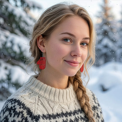 Blonde woman wearing the red mitten earring in a snowy winter landscape, dressed in a warm Nordic knit sweater. Handmade in Finland by byMinta.