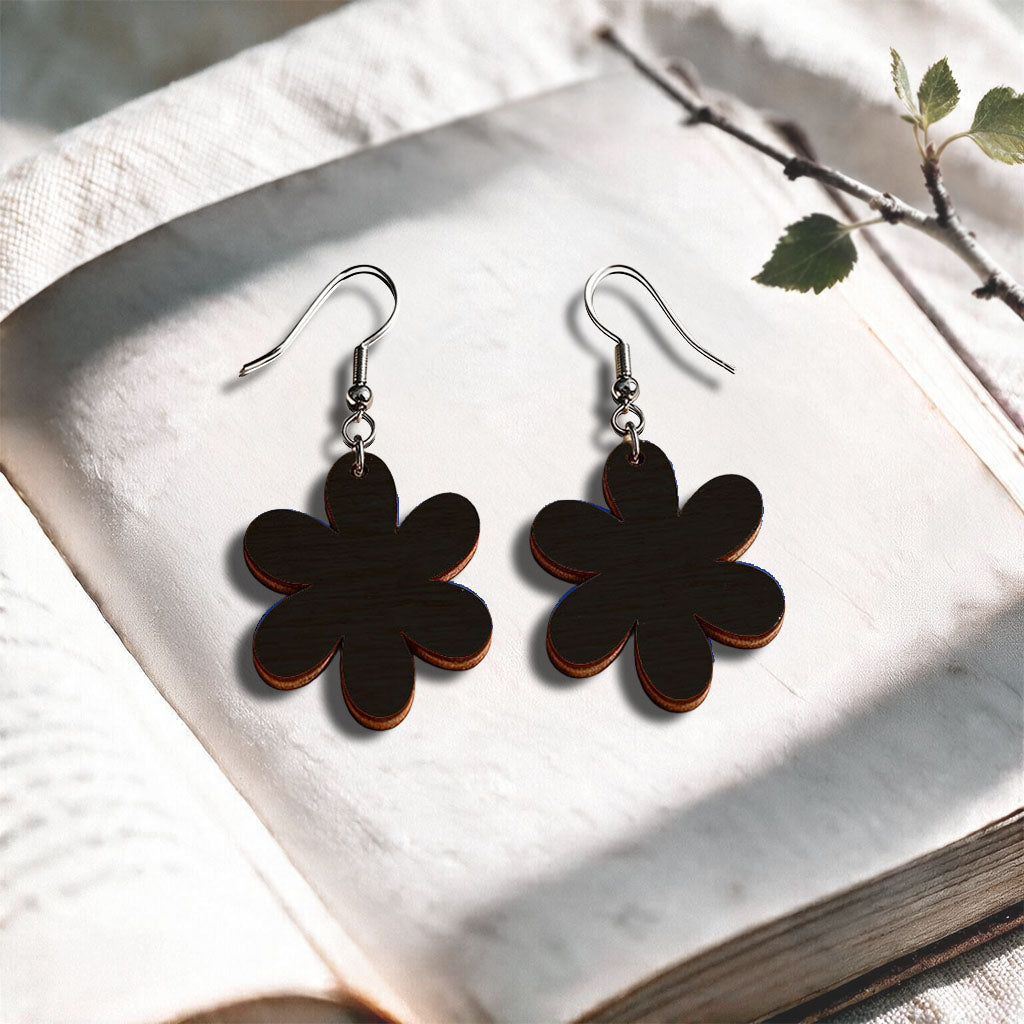 Black Daisy plywood earrings made in Finland, photographed on a vintage book in natural sunlight