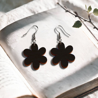 Black Daisy plywood earrings made in Finland, photographed on a vintage book in natural sunlight