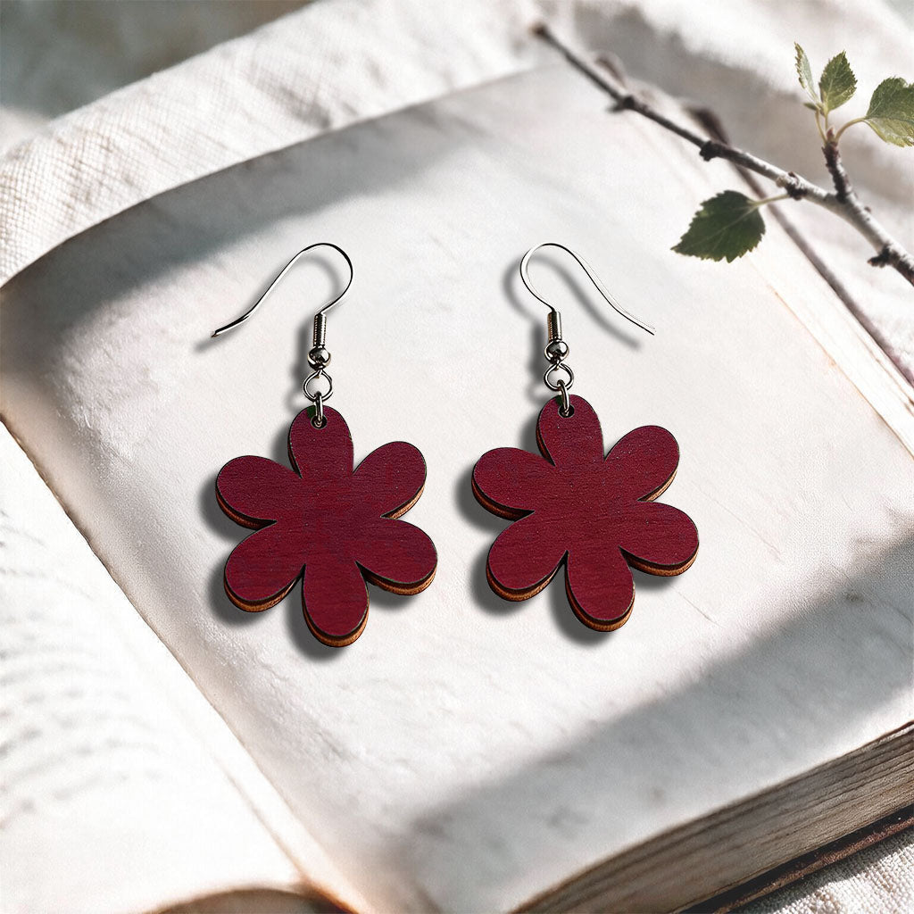 Rust red Daisy plywood earrings made in Finland, photographed on a vintage book in natural sunlight