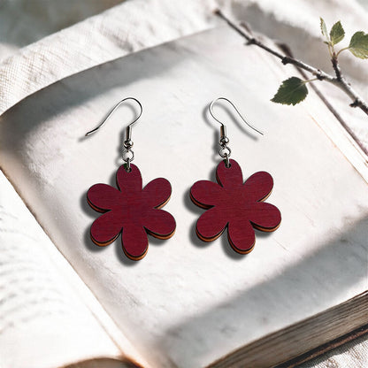 Rust red Daisy plywood earrings made in Finland, photographed on a vintage book in natural sunlight