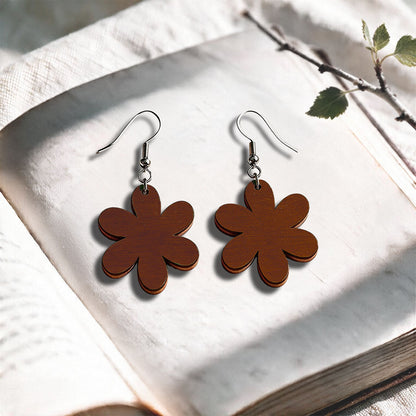Walnut Daisy plywood earrings made in Finland, photographed on a vintage book in natural sunlight