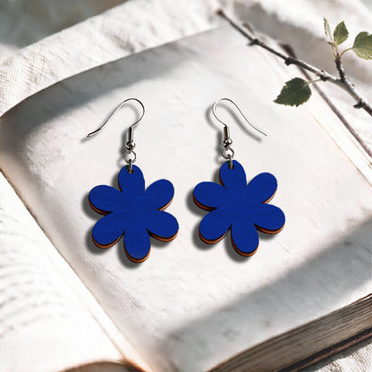 Blue Daisy plywood earrings made in Finland, photographed on a vintage book in natural sunlight