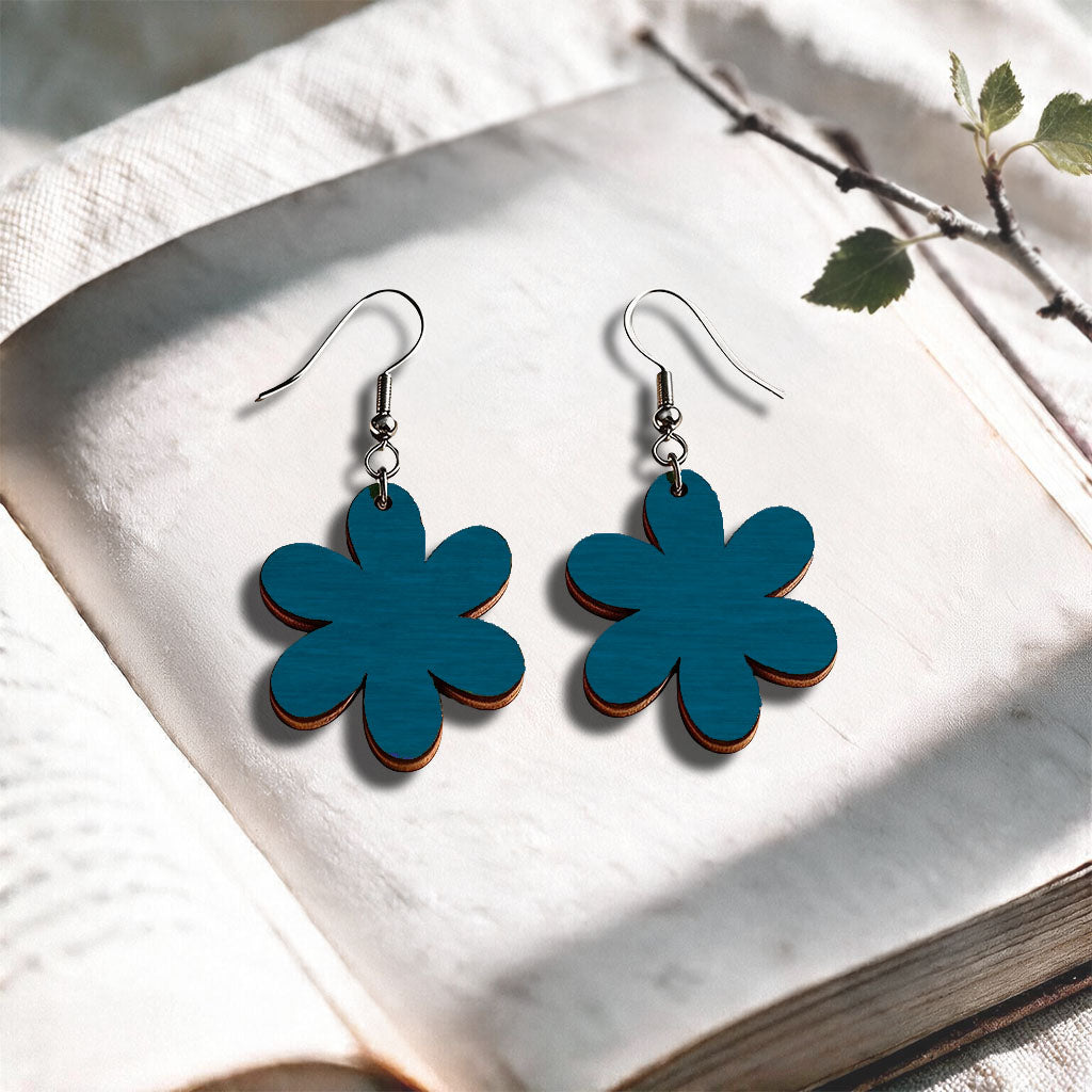 Petrol Daisy plywood earrings made in Finland, photographed on a vintage book in natural sunlight