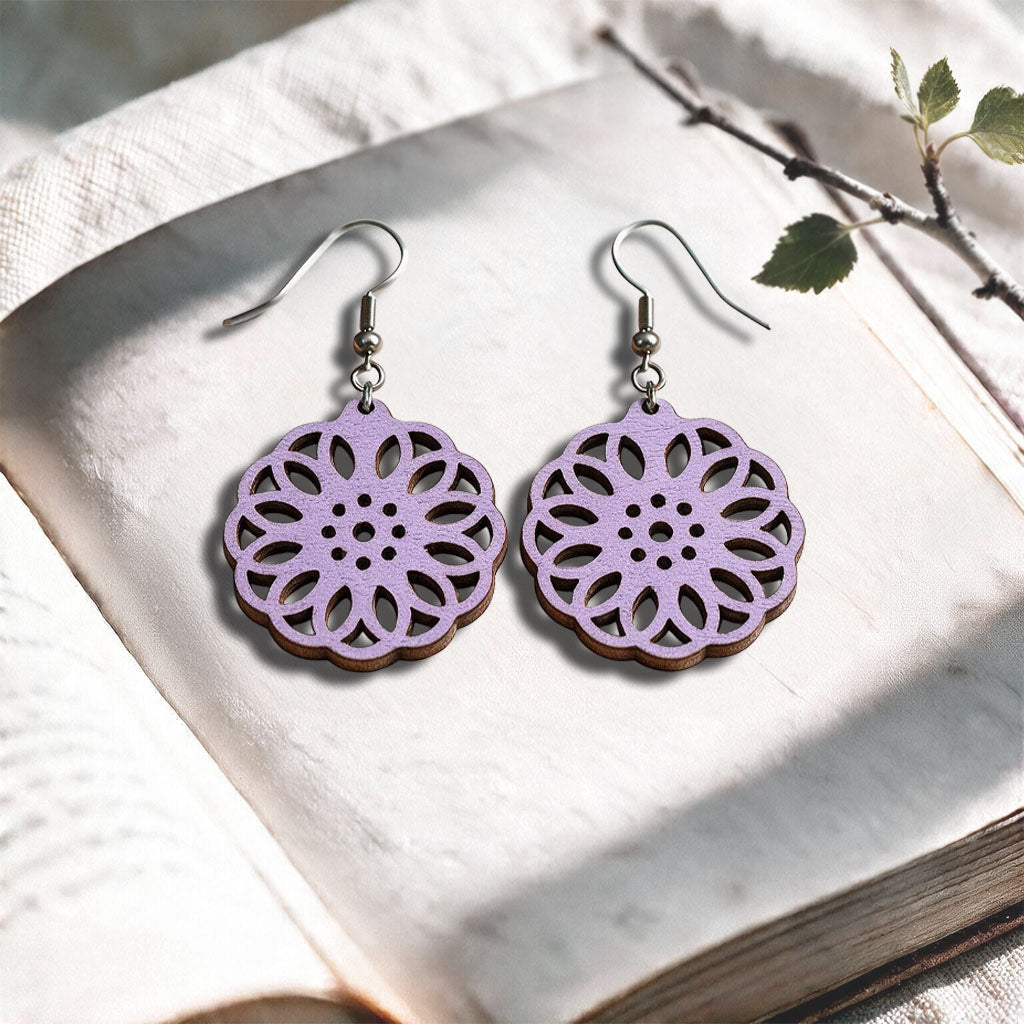 Lavender Kaleidoscope plywood earrings made in Finland, photographed on a vintage book in natural sunlight