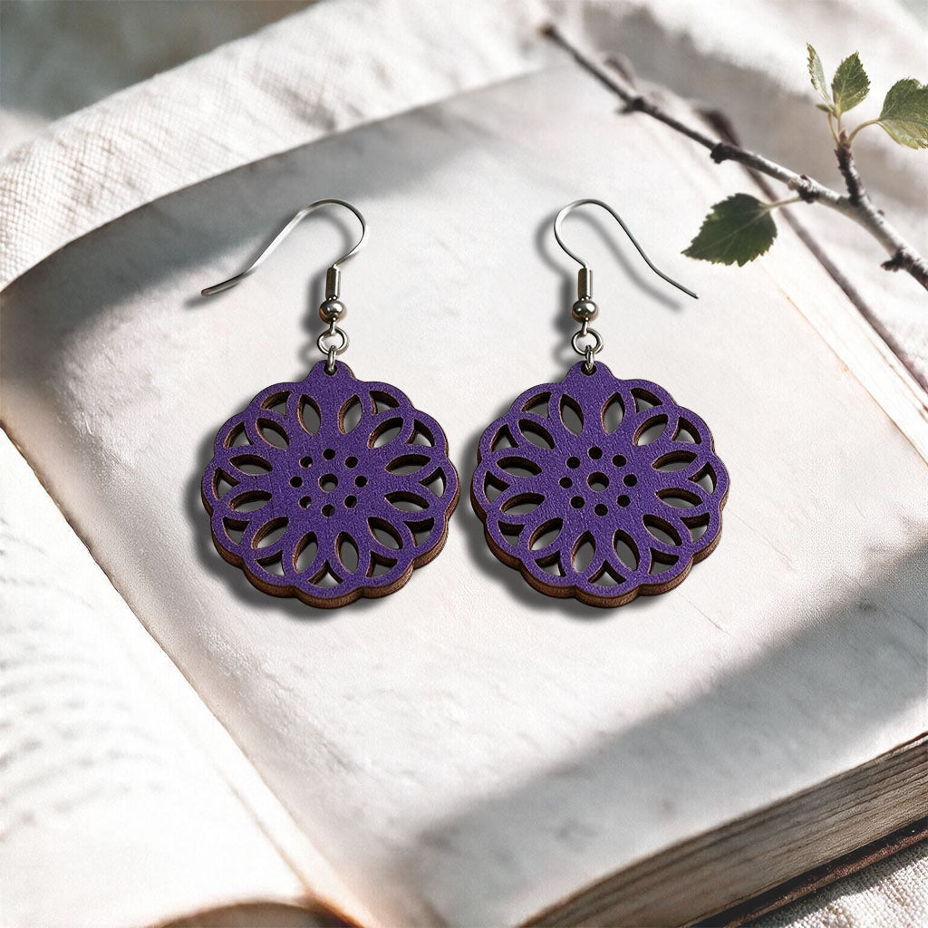 Plum Kaleidoscope plywood earrings made in Finland, photographed on a vintage book in natural sunlight