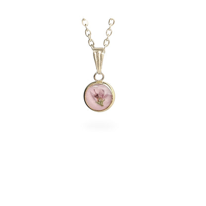 Handmade round botanical necklace with a real heather flower preserved inside resin. Delicate gold-tone pendant with a soft pink background and fine chain on a clean white background, handcrafted in Finland.