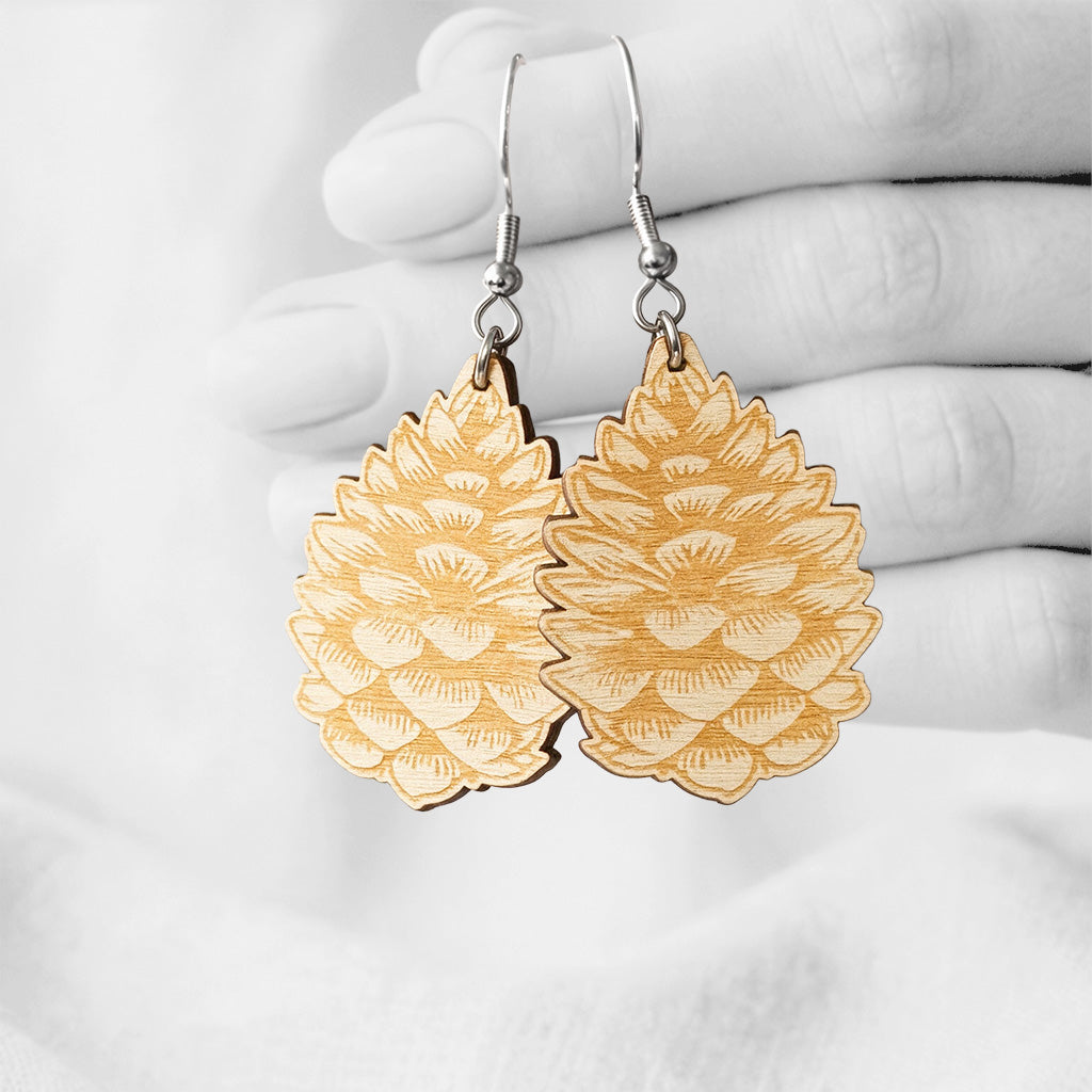 Engarved plywood Käpy (Pinecone) earrings made in Finland, photographed against a black and white background of a hand.