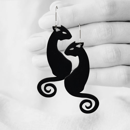 Black Kattimus (Cat) silicone earrings made in Finland, photographed against a black and white background of a hand.