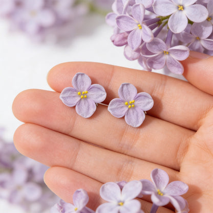 handmade lilac flower stud earrings on hand with lilac blossoms background byMinta