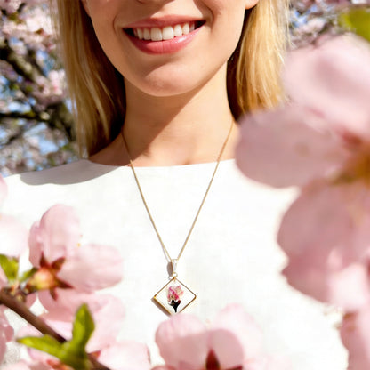 Scandinavian woman wearing a handmade cherry blossom necklace on a delicate chain, photographed among soft pink cherry blossoms in bright natural daylight. Botanical jewelry with a light and airy spring atmosphere.