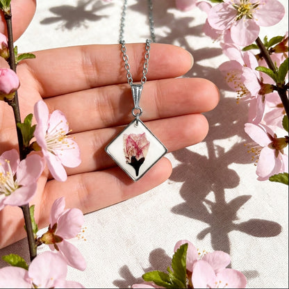 Close-up of cherry blossom pendant necklace with stainless steel chain held among blooming flowers