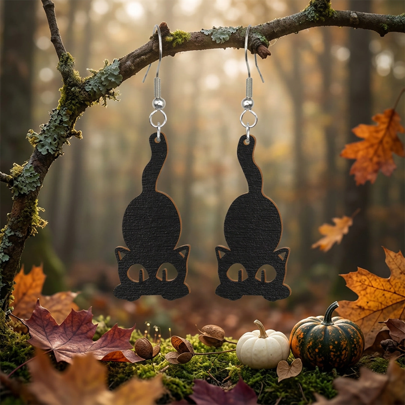 Black Cat Earrings hanging from a moss-covered branch in an autumn forest.