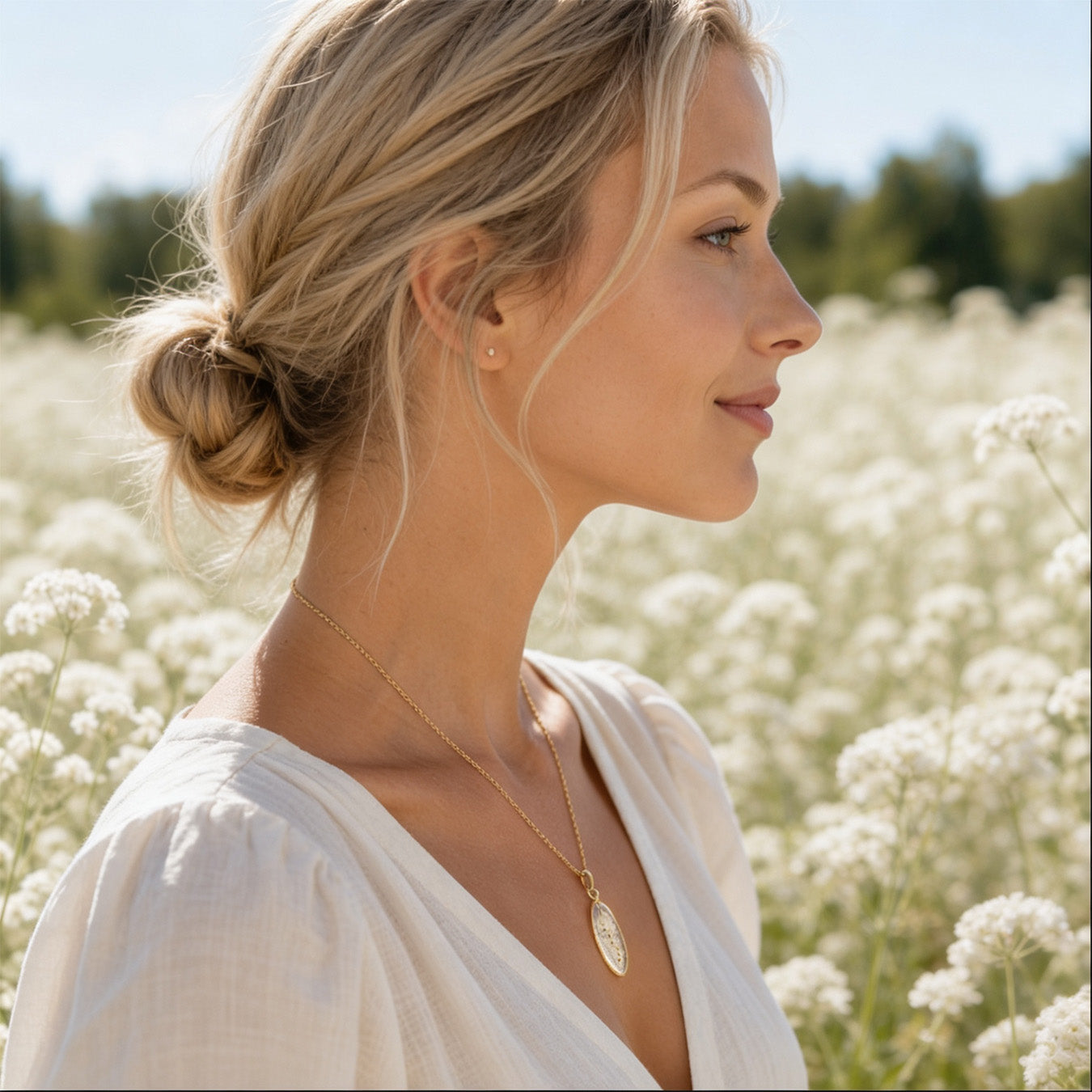 Scandinavian woman wearing a handmade botanical necklace with real pressed cow parsley flowers preserved in clear resin. Portrait photographed in a field of white cow parsley blooms in bright natural daylight with a soft and airy Nordic summer atmosphere.