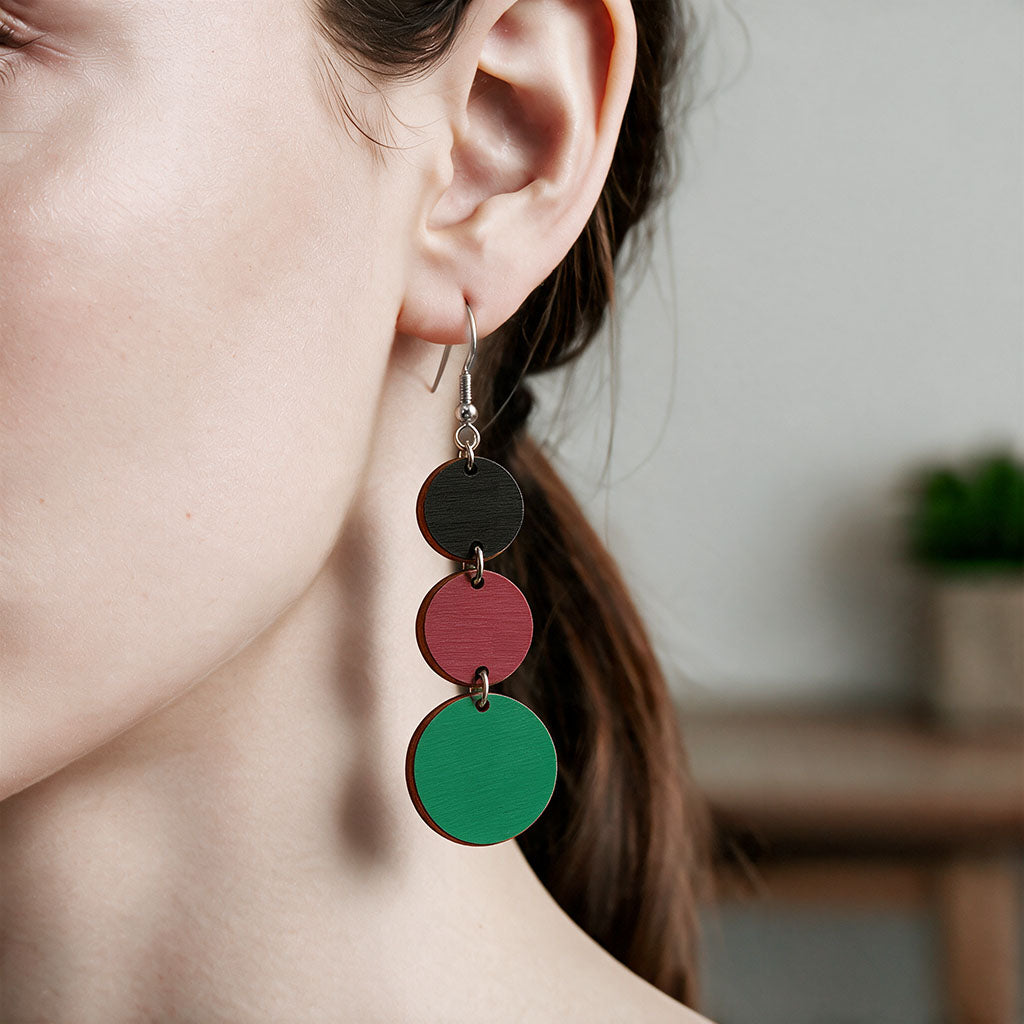 Black, rust and green Saippuakupla plywood earrings made in Finland, shown worn on the ear to demonstrate size and scale