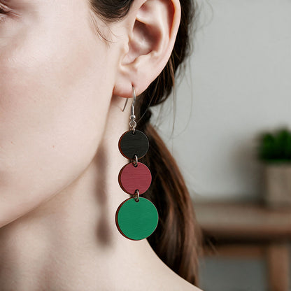 Black, rust and green Saippuakupla plywood earrings made in Finland, shown worn on the ear to demonstrate size and scale