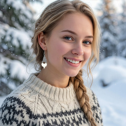 Smiling blonde woman wearing silver and white Christmas gnome earrings in a snowy winter landscape, dressed in a cozy Nordic knit sweater. Handmade in Finland by byMinta.