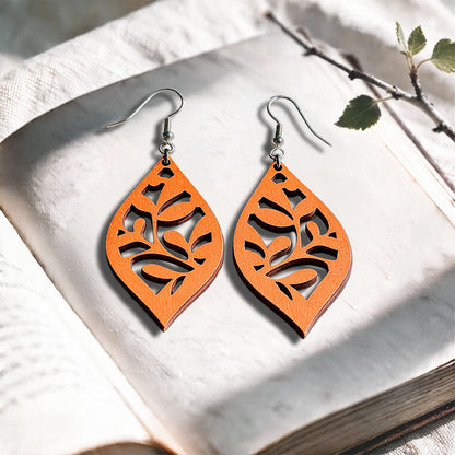 Papaya Vine plywood earrings made in Finland, photographed on a vintage book in natural sunlight