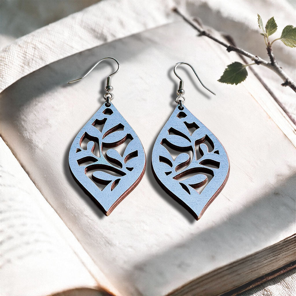 Light Blue Vine plywood earrings made in Finland, photographed on a vintage book in natural sunlight