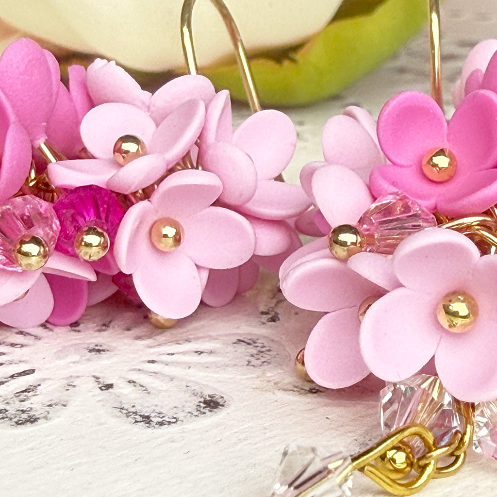 Close-up of handcrafted pink flower earrings showing delicate layered petals, gold-colored accents, and crystal bead details. Handmade in Finland.