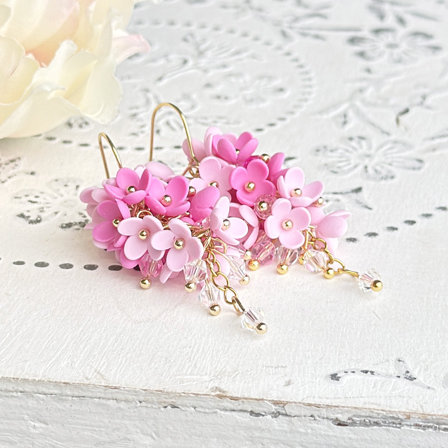 Handcrafted pink flower cluster earrings on rustic white wood. Lightweight floral earrings with crystal bead details, handmade in Finland.