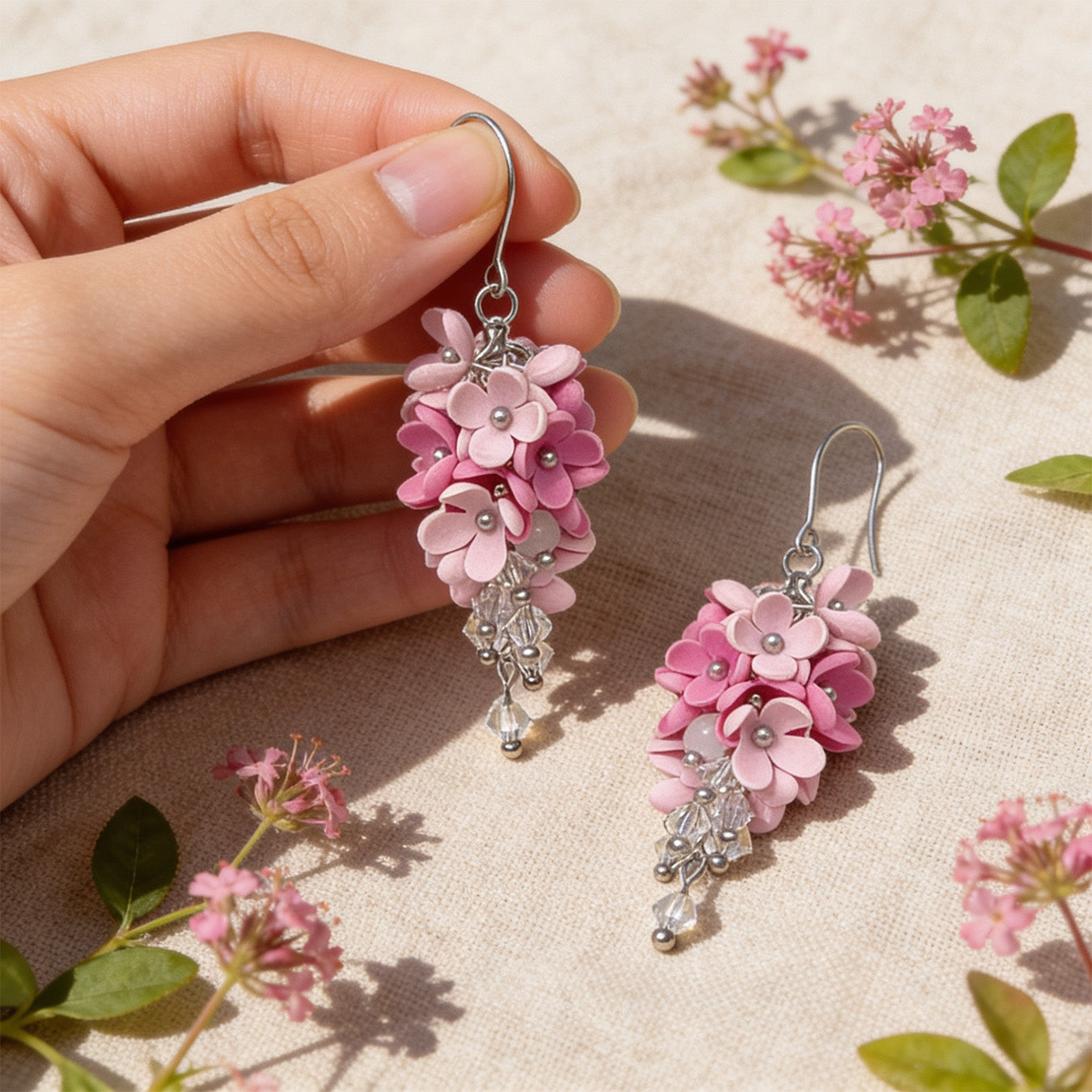 Flower Cloud Earrings photographed in soft natural light, with one earring gently held by hand for scale and surrounded by delicate pink blossoms. Handmade in Finland by byMinta.