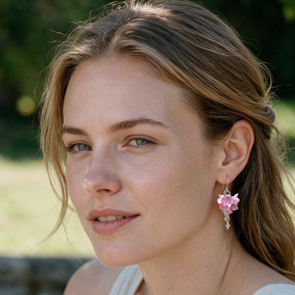Pink Kukkaverso flower earrings worn by a woman outdoors in natural summer light, handmade in Finland