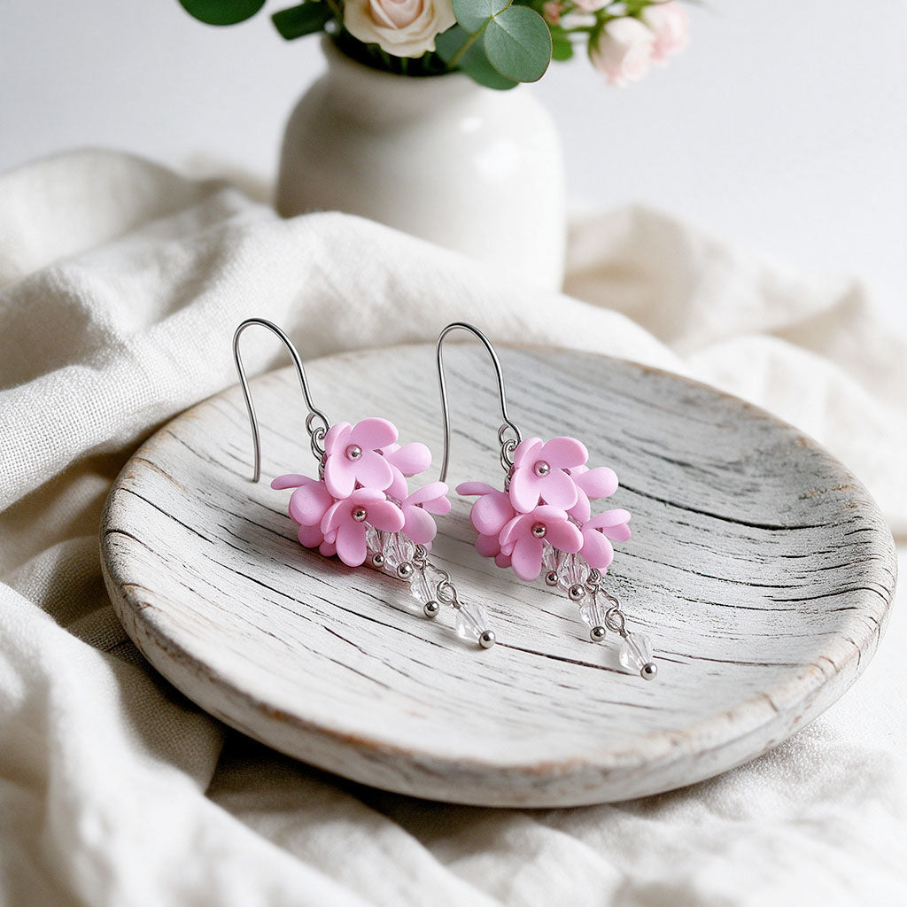 Pink Kukkaverso earrings with small handmade flowers and clear crystals, photographed on a light vintage plate