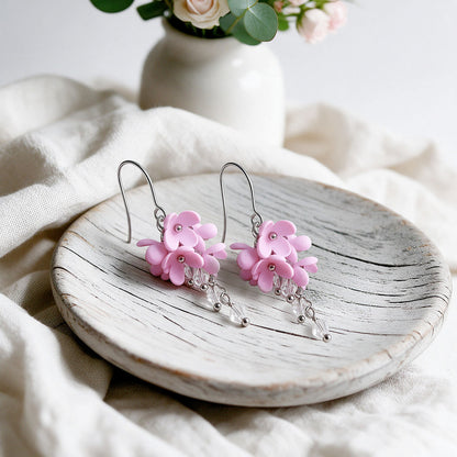 Pink Kukkaverso earrings with small handmade flowers and clear crystals, photographed on a light vintage plate