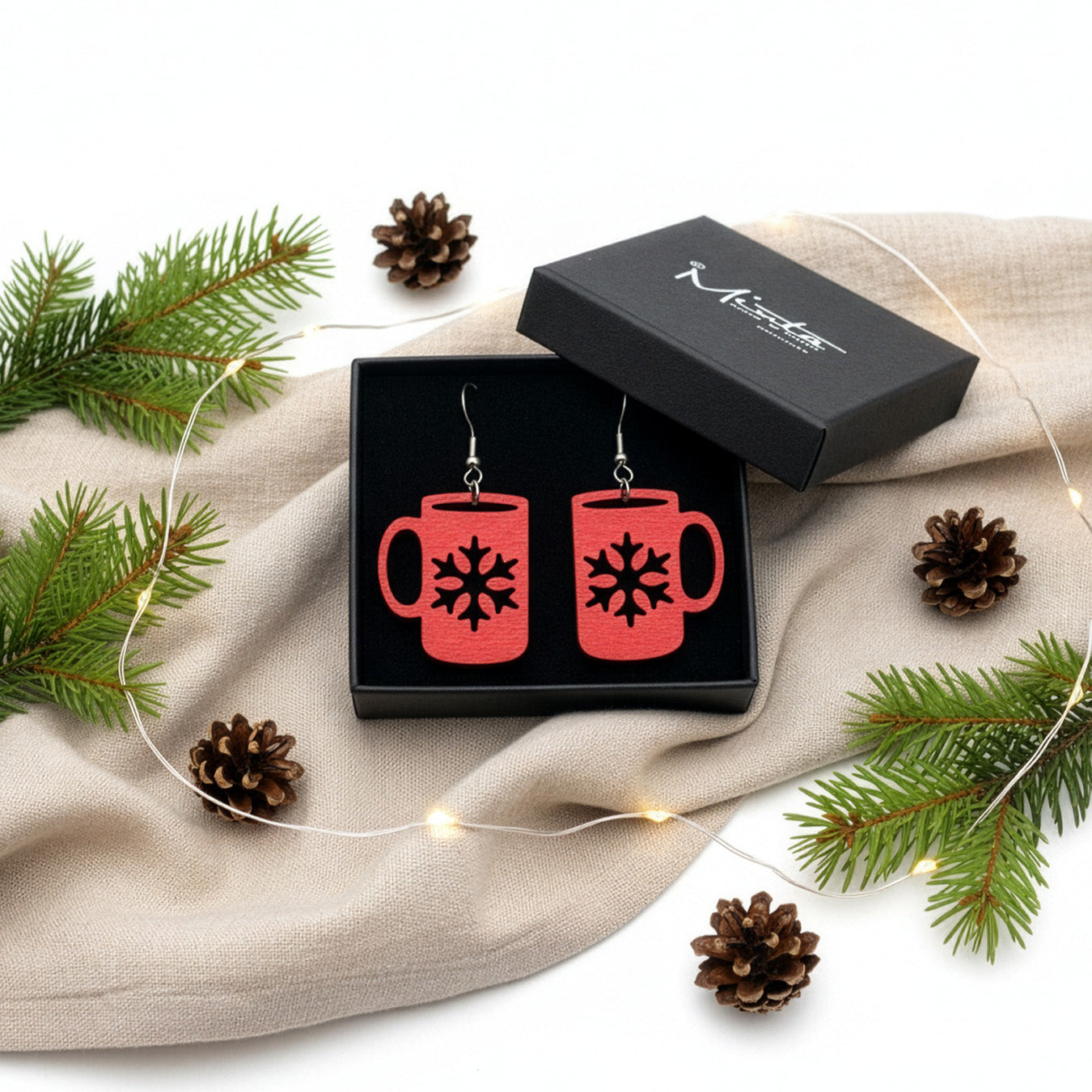 Red mug earrings presented in a gift box with pine branches, pinecones, and soft lights, creating a warm Christmas atmosphere. Handmade in Finland by byMinta.