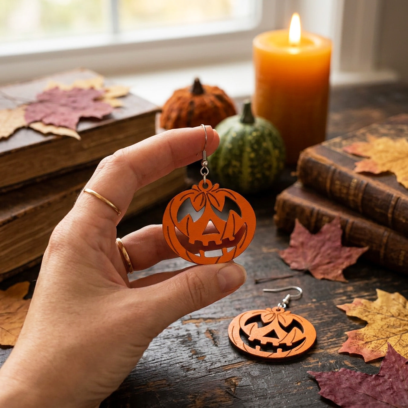 Hand holding pumpkin earrings with jack-o'-lantern design, handmade in Finland.
