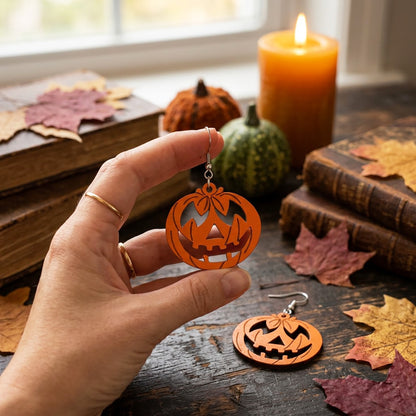 Hand holding pumpkin earrings with jack-o'-lantern design, handmade in Finland.